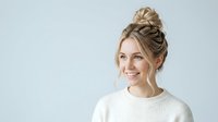 Young woman with blonde hair styled in a top bun, fair complexion, wearing a cream ribbed sweater against a light background. Suitable for lifestyle, beauty, and wellness marketing materials.
