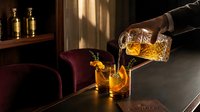 Elegant whiskey pouring from crystal decanter into glass on wooden table in warm sunlight creating sophisticated bar atmosphere for luxury dining concepts.