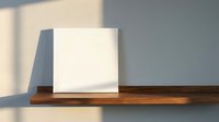 Blank white canvas or poster mockup on wooden shelf against gray wall with natural window light shadows for artwork display and presentation.