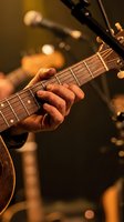 Close-up of guitarist hand playing acoustic guitar with warm stage lighting and blurred microphone in background during live music performance.