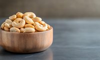 Raw cashew nuts in wooden bowl on dark background with copy space, healthy vegetarian protein snack for nutrition and diet concept.