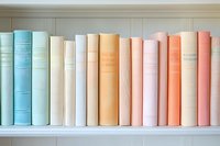 Row of vintage hardcover books arranged on white wooden shelf in pastel colors - blue, beige, peach and coral spines create soft color gradient pattern.