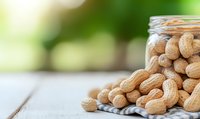 Raw peanuts in clear glass jar on rustic wooden table with soft green bokeh background, healthy protein-rich snack for nutrition and cooking.