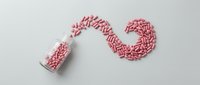 Red and white capsules spilling from bottle creating flowing stream pattern on white background for pharmaceutical medical healthcare design.
