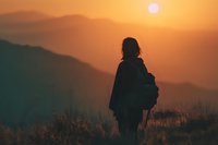 Silhouette of female hiker with backpack watching sunrise over mountain ranges. Outdoor adventure and travel concept for wellness and exploration content.