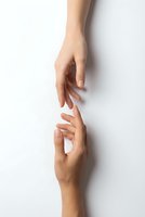 Two hands reaching toward each other in gentle touching gesture on white background symbolizing connection, support, help and human relationships.