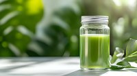 Green fresh smoothie or juice in glass mason jar on white table with natural green blurred background, healthy detox drink concept.