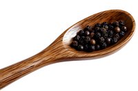 Whole black peppercorns in wooden spoon on white background, macro food photography for cooking, culinary and spice marketing materials.