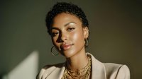 Confident African American woman with short natural hair, gold jewelry, and beige blazer in dramatic lighting, portraying elegance and professionalism.