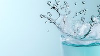 Refreshing water splash in glass with dynamic droplets and ripples against light blue background, capturing liquid motion in high-speed photography.