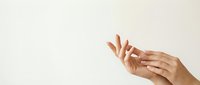 Elegant female hands with natural manicure applying moisturizer cream on neutral beige background for skincare beauty routine and cosmetic advertising.