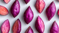 Fresh purple sweet potatoes sliced to reveal vibrant pink flesh pattern on white background, organic healthy food ingredients for cooking and nutrition.