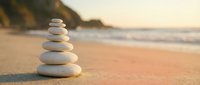 Balanced stone stack on sandy beach at sunset creating peaceful zen meditation scene for wellness and mindfulness concepts.