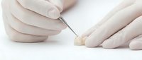 Dental technician in gloves holding ceramic tooth crown with tool on white background, showcasing prosthetic dentistry and dental restoration work.