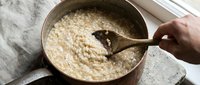 Creamy risotto being stirred in a stainless steel pot with wooden spoon, ideal for cooking and food preparation content.