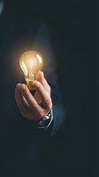 Businessman holding glowing incandescent bulb against dark background, symbolizing innovation, creativity, and bright ideas for business solutions and entrepreneurship concepts.