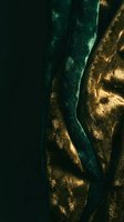 Luxurious emerald green and gold metallic fabric with flowing folds and dramatic lighting creating elegant textile waves for fashion and interior design.