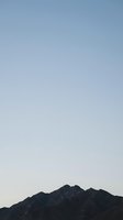Serene mountain silhouette against clear sky at dusk, minimalist landscape with dark rocky peaks and soft gradient horizon for peaceful backgrounds.