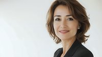 Professional middle-aged woman with brown wavy bob hairstyle smiling confidently against white background, wearing black blazer for corporate headshot.