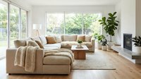 Spacious modern living room with beige sectional sofa, natural light from large windows, wooden flooring, potted plants, and contemporary home decor for interior design inspiration.