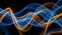 Glowing blue and golden light waves flowing across dark background, creating dynamic energy patterns for technology and innovation concepts.