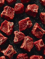 Raw beef chunks with marbling on dark background, fresh cut meat pieces with fat layers and salt crystals, ready for cooking and food preparation.