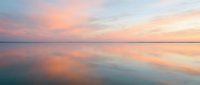 Serene sunset over calm water with soft pink and orange hues reflecting on glassy surface, ideal for backgrounds and nature themes.
