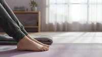 Woman practicing yoga meditation in peaceful home studio with natural light streaming through windows creating serene wellness atmosphere.