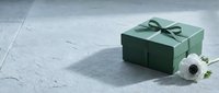 Green gift box with satin ribbon bow on concrete surface next to white flowers for special occasions and celebrations.