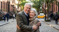 Happy senior couple embracing on urban street with brownstone buildings. Elderly man and woman showing love and affection in city neighborhood setting.