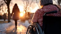 Young woman walking away in winter park at sunset while person in wheelchair watches, creating poignant moment of solitude and reflection against golden sunlight and snowy landscape.