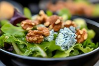 Fresh green salad with crunchy walnuts and crumbled blue cheese on black plate, macro food photography with selective focus and natural lighting.