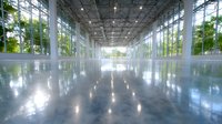 Modern empty warehouse interior with polished concrete floor, glass walls, metal columns and natural light streaming through windows creating reflections.