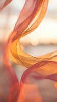 Flowing orange and pink silk ribbons creating elegant curves and waves against soft blurred background for luxury design projects.