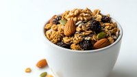 Healthy mixed nuts and dried fruits in white bowl on clean background for nutritious snacking and cooking recipes.