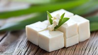 Fresh tofu cubes garnished with white jasmine flowers and green leaves arranged on rustic wooden surface, soft focus composition highlighting protein-rich Asian cuisine.