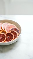 Sliced grapefruit and blood orange citrus fruits arranged in white ceramic bowl on marble surface for food styling and culinary design.