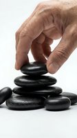 Caucasian hand stacking smooth black basalt stones on white background, symbolizing balance, mindfulness, and zen meditation for wellness and spa concepts.
