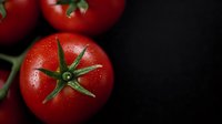 Fresh ripe red tomatoes with water drops and green stems on dark background, macro shot showing texture and natural moisture for food photography and marketing.