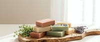 Handmade natural soap bars with herbs on wooden board. Organic skincare products for spa treatments and daily cleansing routines at home.