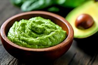 Fresh guacamole dip in rustic wooden bowl with ripe avocado on dark wooden table, traditional Mexican appetizer with creamy texture and vibrant green color.