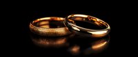Two wedding rings in gold and silver on dark background with dramatic lighting and reflection, symbolizing marriage, commitment and eternal love.