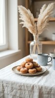 Fresh homemade donuts on ceramic plate with coffee cup and pampas grass decoration in cozy kitchen interior for breakfast and bakery concepts.