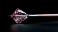 Sharp metallic hunting broadhead arrow tip with intricate geometric design and textured grip shaft against dark background, dramatic lighting highlights details.