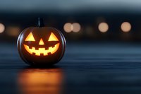 Glowing carved pumpkin with classic jack o'lantern face illuminated from within against dark background with soft bokeh lights creating spooky Halloween atmosphere.