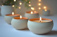 Glowing white ceramic candles with warm flames in round pottery holders create cozy atmosphere against soft bokeh lights background. Perfect for spa and wellness.