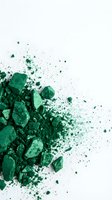 Crushed green powder and pigment particles dispersing across white background, suitable for cosmetics, art, and design projects.
