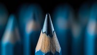 Sharp graphite pencil tip emerging from row of blue wooden pencils in soft focus background, macro photography with selective depth of field.