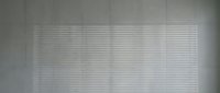 Sunlight streaming through white horizontal blinds creating striped shadow patterns on wall. Natural lighting effect for interior design and home decor projects.