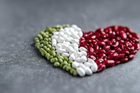 Heart shape made from colorful dried beans in green, white and red arranged on dark concrete background, selective focus with blurred edges.